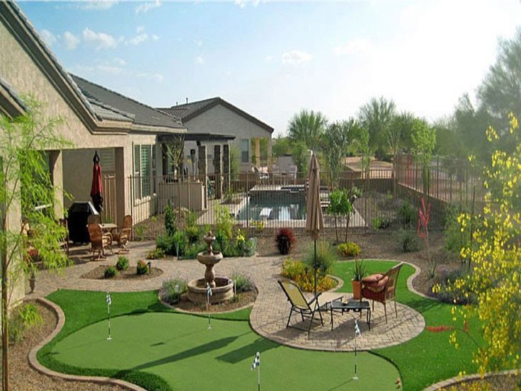 A backyard in Atlantic Beach features a putting green, a patio with outdoor furniture, and a swimming pool enclosed by a metal fence. This recent outdoor area upgrade includes turf installation, trees, shrubs, and gravel pathways. Neighboring houses frame the setting under a clear sky.