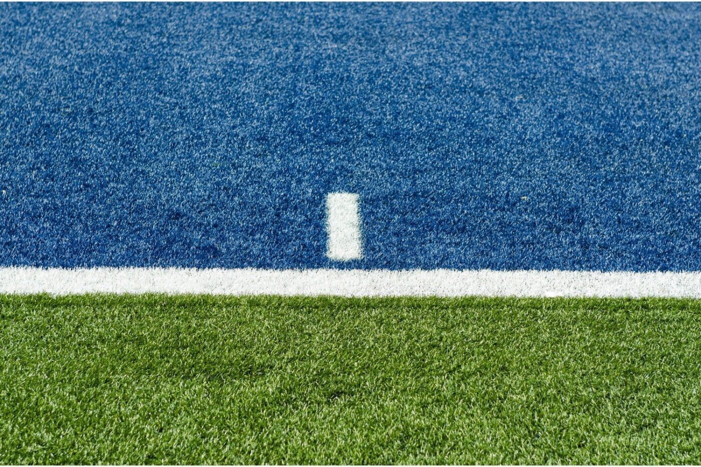 Close-up view of an artificial turf field featuring three distinct sections: the bottom third is green, the middle section is white, and the top is blue. A white line and a vertical white hash mark intersect between the blue and white sections—expertly crafted by Jacksonville Artificial Turf.