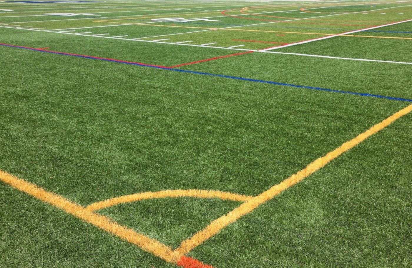 A close-up view of a synthetic turf field marked with various colored lines for different sports. Yellow, red, blue, and white lines intersect across the green surface, showing boundaries and play areas for activities like soccer, football, and lacrosse—an ideal upgrade for St. Johns homeowners seeking artificial turf installation to enhance their outdoor space.