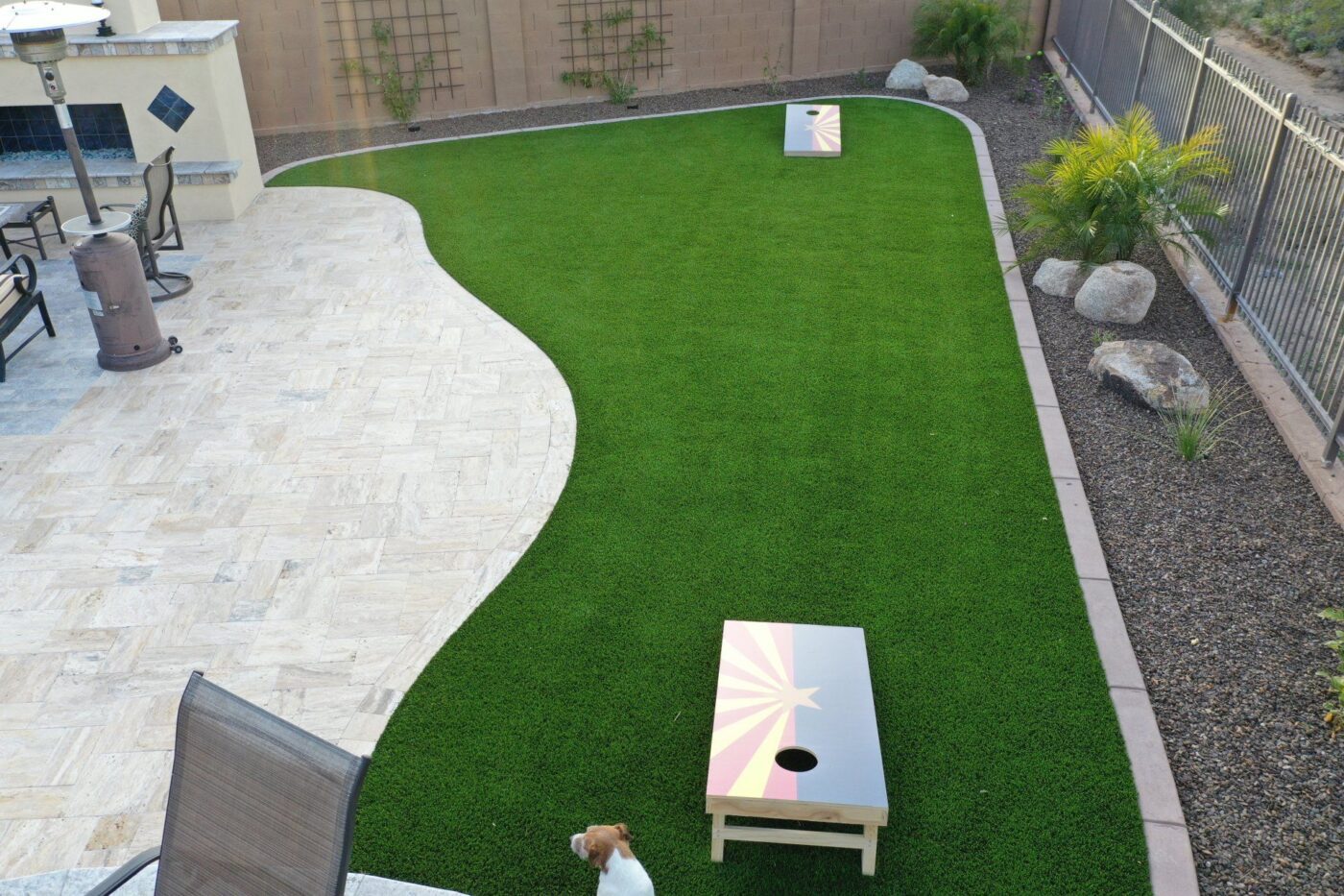 Close-up of a lawn with vibrant green grass. In the background, there are modern buildings and a black fence, slightly out of focus. The sky is clear and blue, suggesting a sunny day. The image captures the texture and detail of Jacksonville Artificial Turf. Get your free quote today!