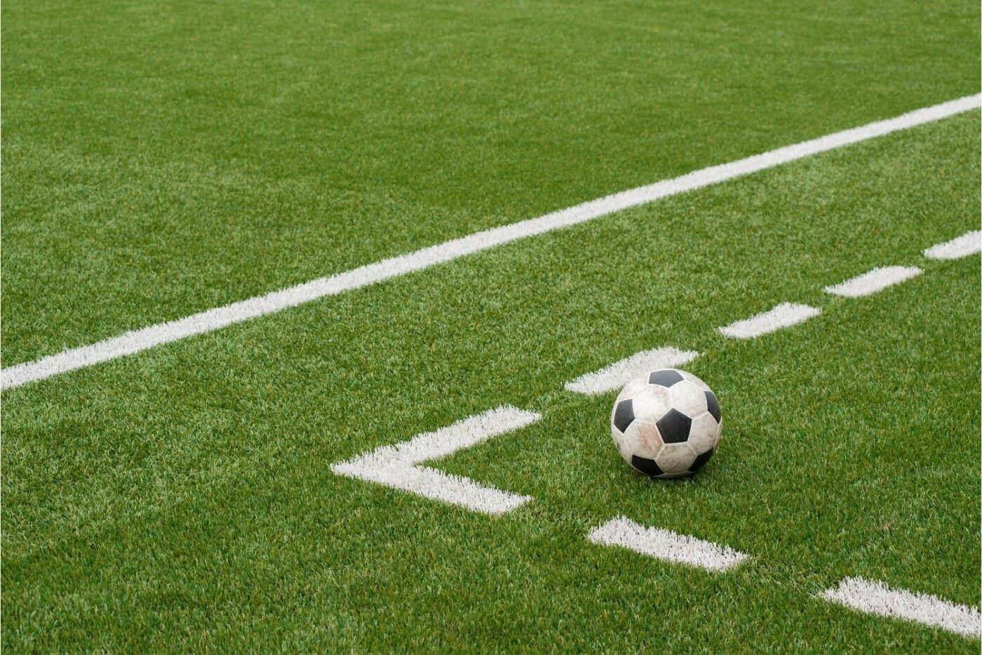 An outdoor rooftop soccer field with green artificial turf offers a dynamic outdoor living space. The field is enclosed by a net and green metal fencing, with buildings and skyscrapers towering in the background under a clear blue sky, showcasing expert fake turf installation.