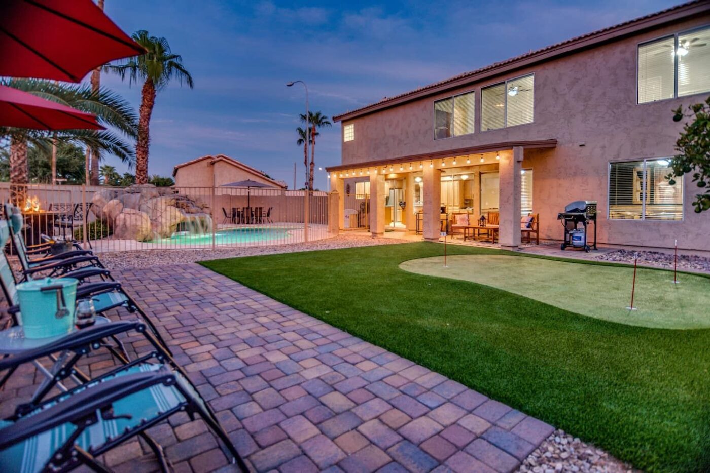 A neatly landscaped backyard in Fernandina Beach features a well-manicured lawn, surrounded by a stone-paved walkway. With a small tree in the center and a high brick wall enclosing the area, this inviting outdoor living space is adorned with bushes and potted plants along the perimeter.